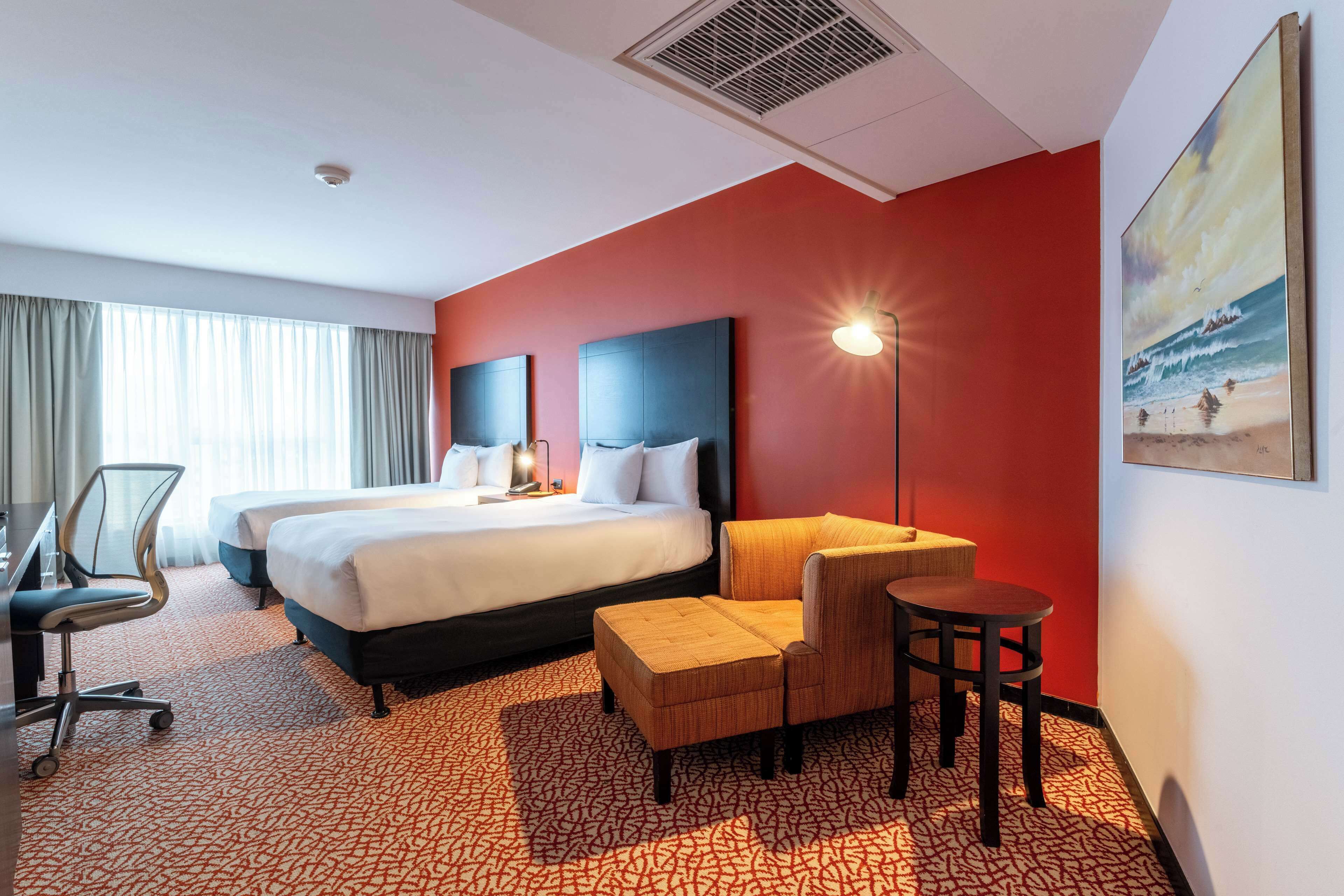 Habitación de hotel con una cama grande, dos mesitas de noche, un escritorio con una silla, un pequeño sofá y una mesa redonda.