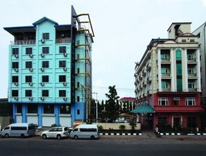 A multi-story building with a blue and white facade, several balconies, and a parking area with cars. - Hotel Glory (Yangon)