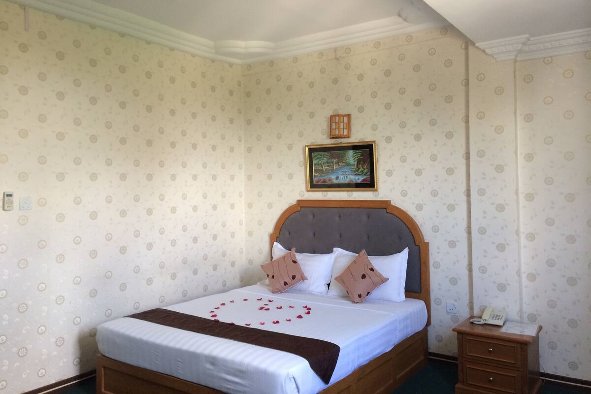 A neatly made bed with a wooden headboard, a bedside table with a phone, and a patterned wallpaper.