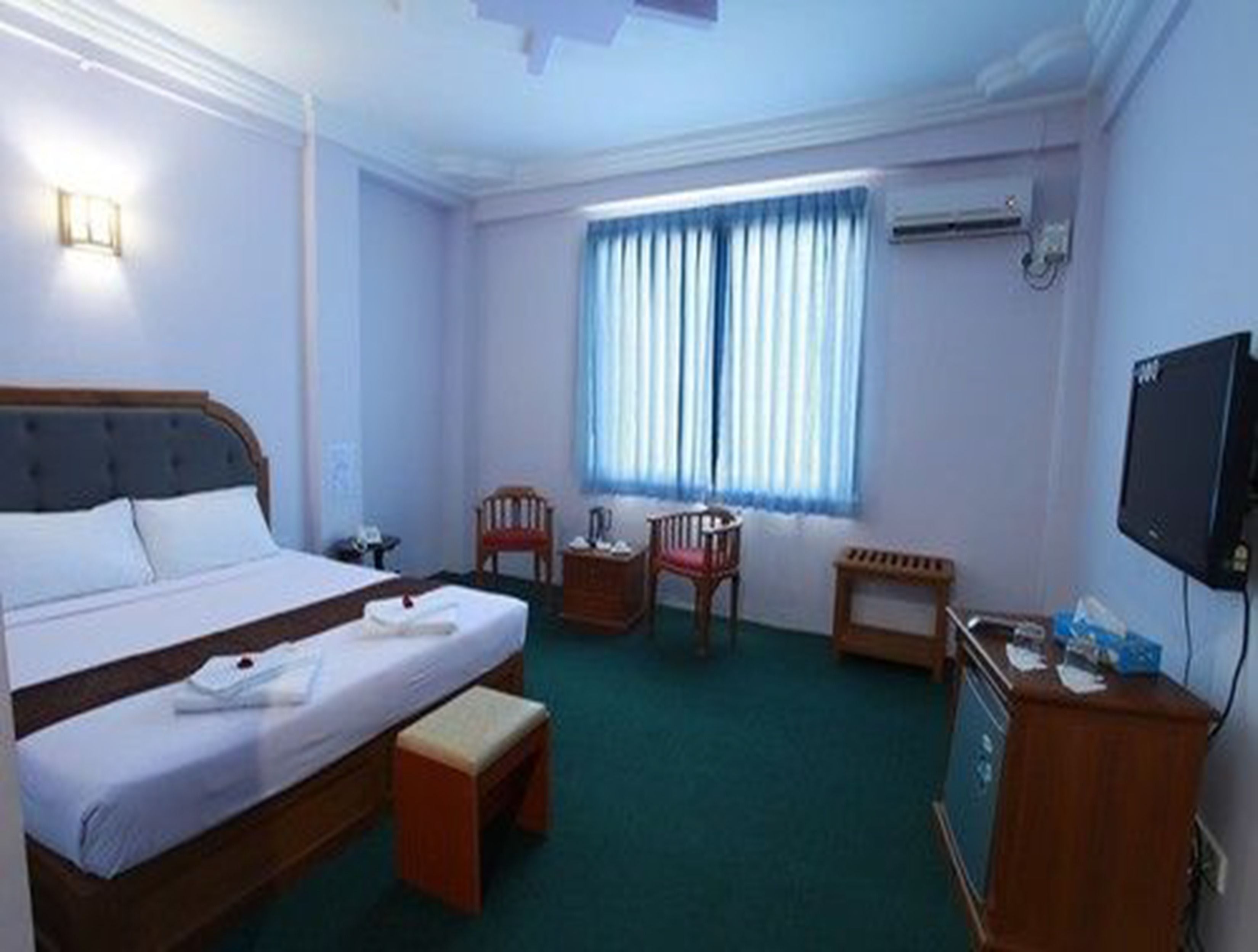 Una habitación de hotel con cama, escritorio, silla, televisor y ventana con cortinas.