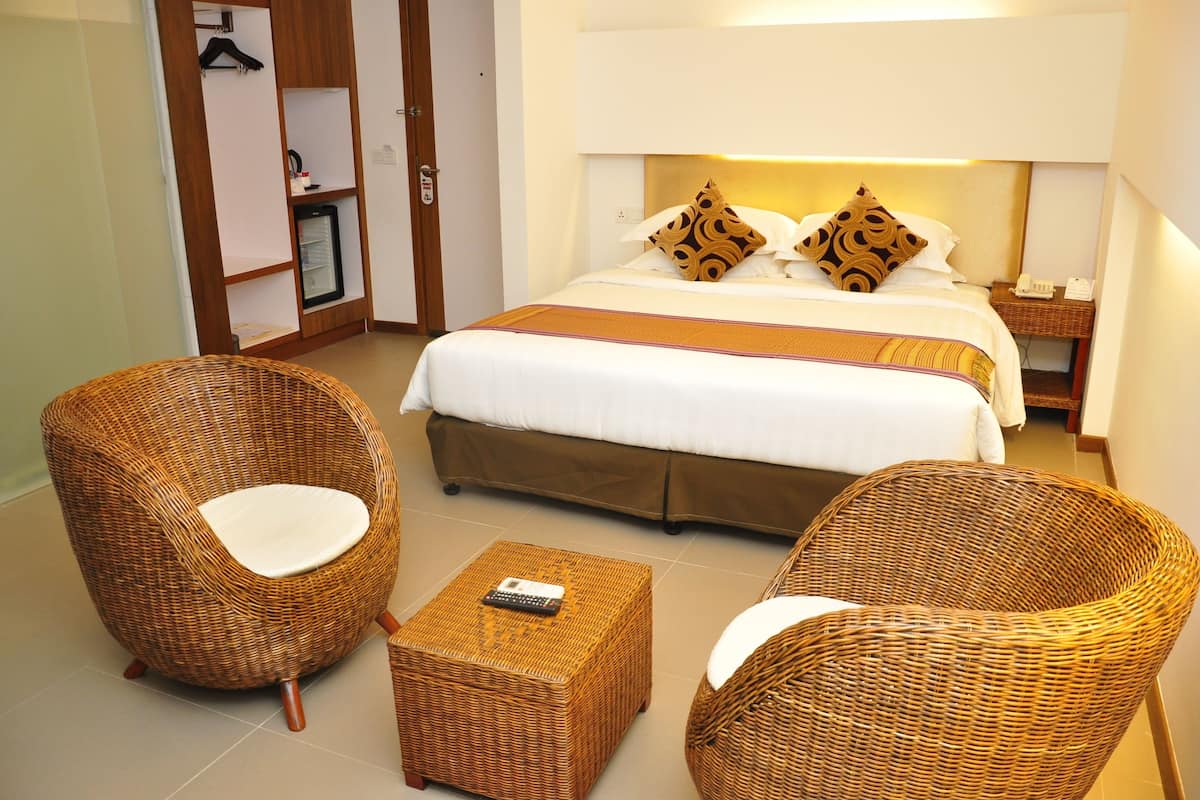 Habitación de hotel con una cama, dos sillas de mimbre, una mesita y una mesita de noche con un teléfono.