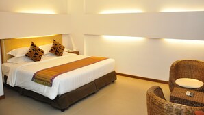 Habitación de hotel con una cama grande, una mesita de noche, una silla de mimbre e iluminación en la pared.