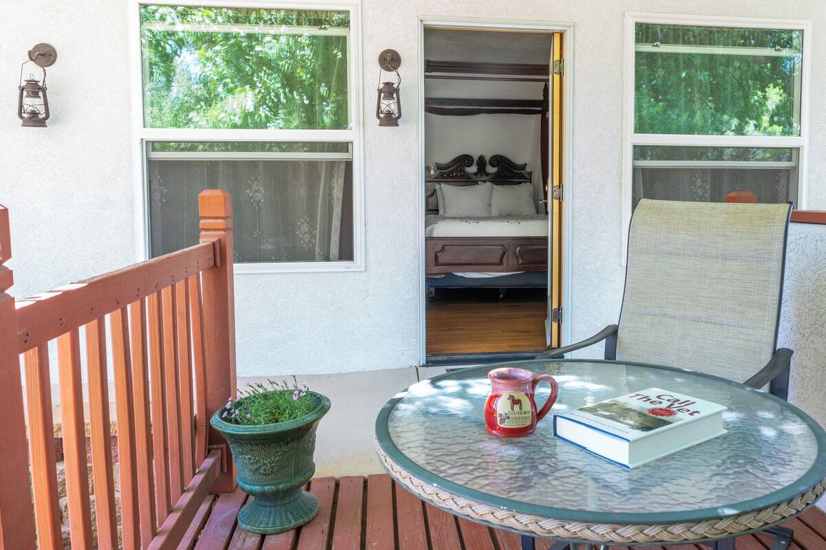 Une table en verre avec un livre et une tasse, une chaise, une plante en pot et une terrasse en bois.
