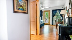 Una habitación con piso de madera, una cama con cubrecama azul, un escritorio con lámpara y un ventilador de techo.
