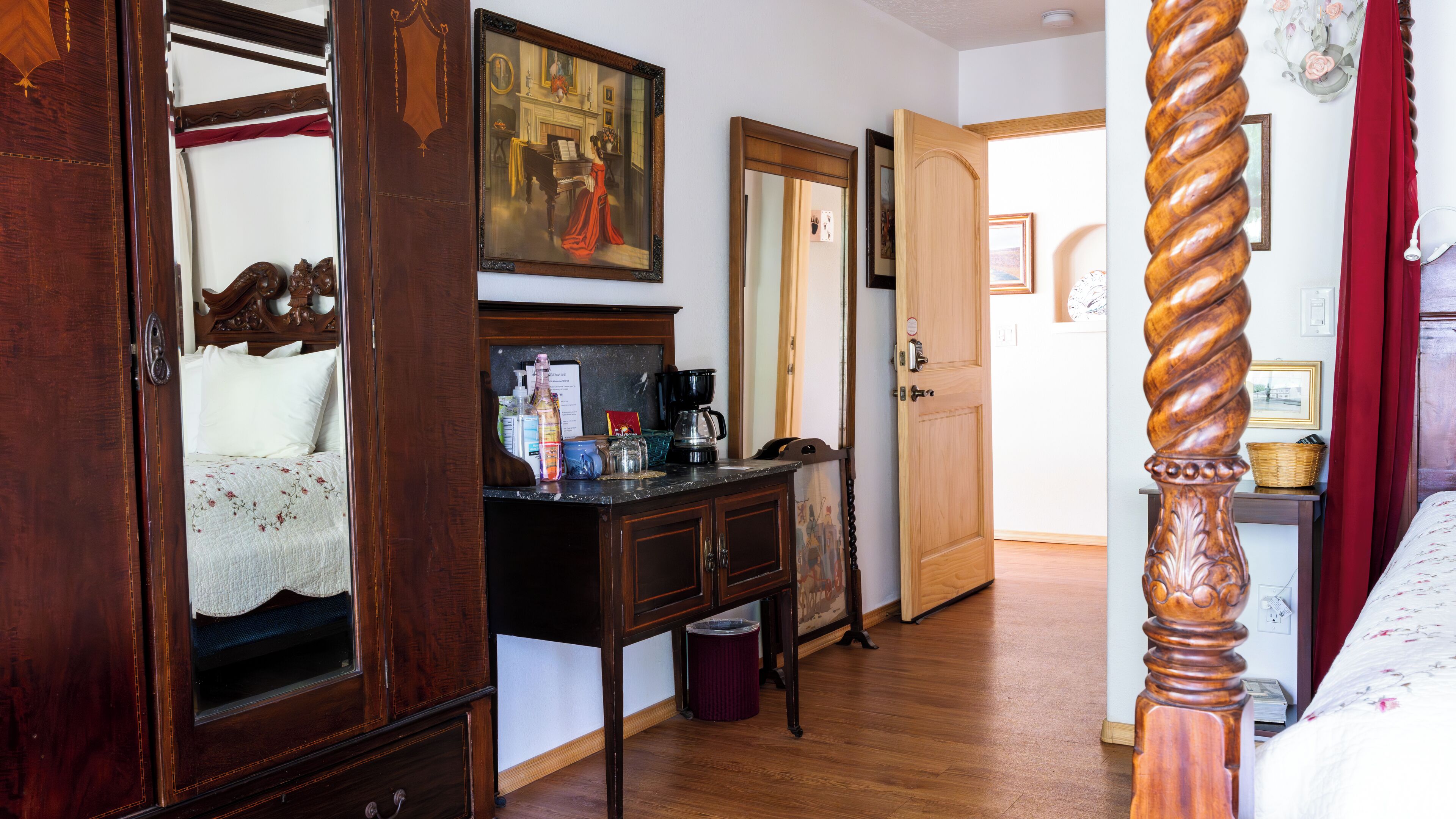 A bedroom with a wooden bed, a dresser with a mirror, a painting on the wall, and a door leading to another room.