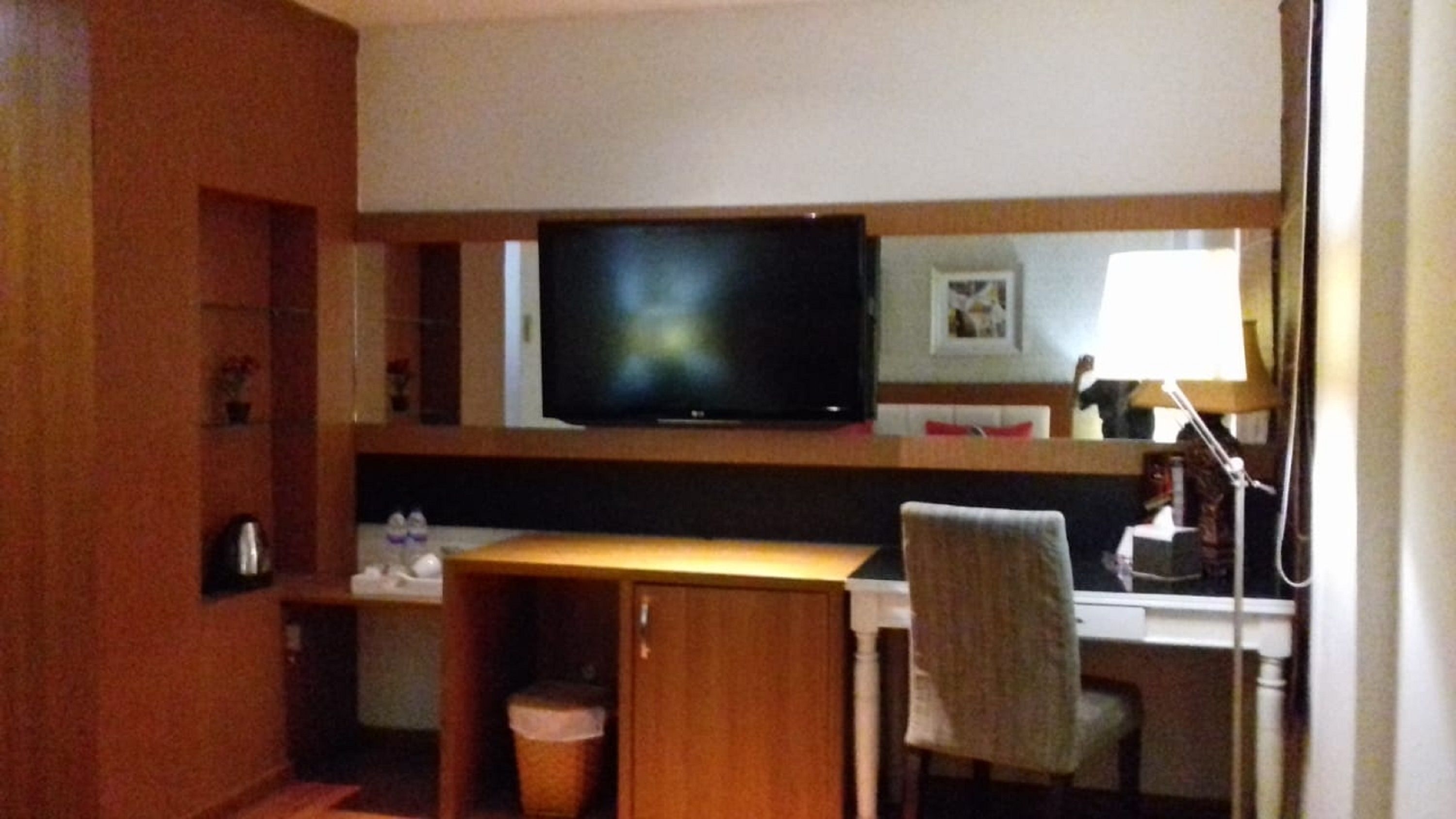 Habitación de hotel con televisor de pantalla plana montado en la pared, un escritorio de madera, una silla y un cesto de basura pequeño.