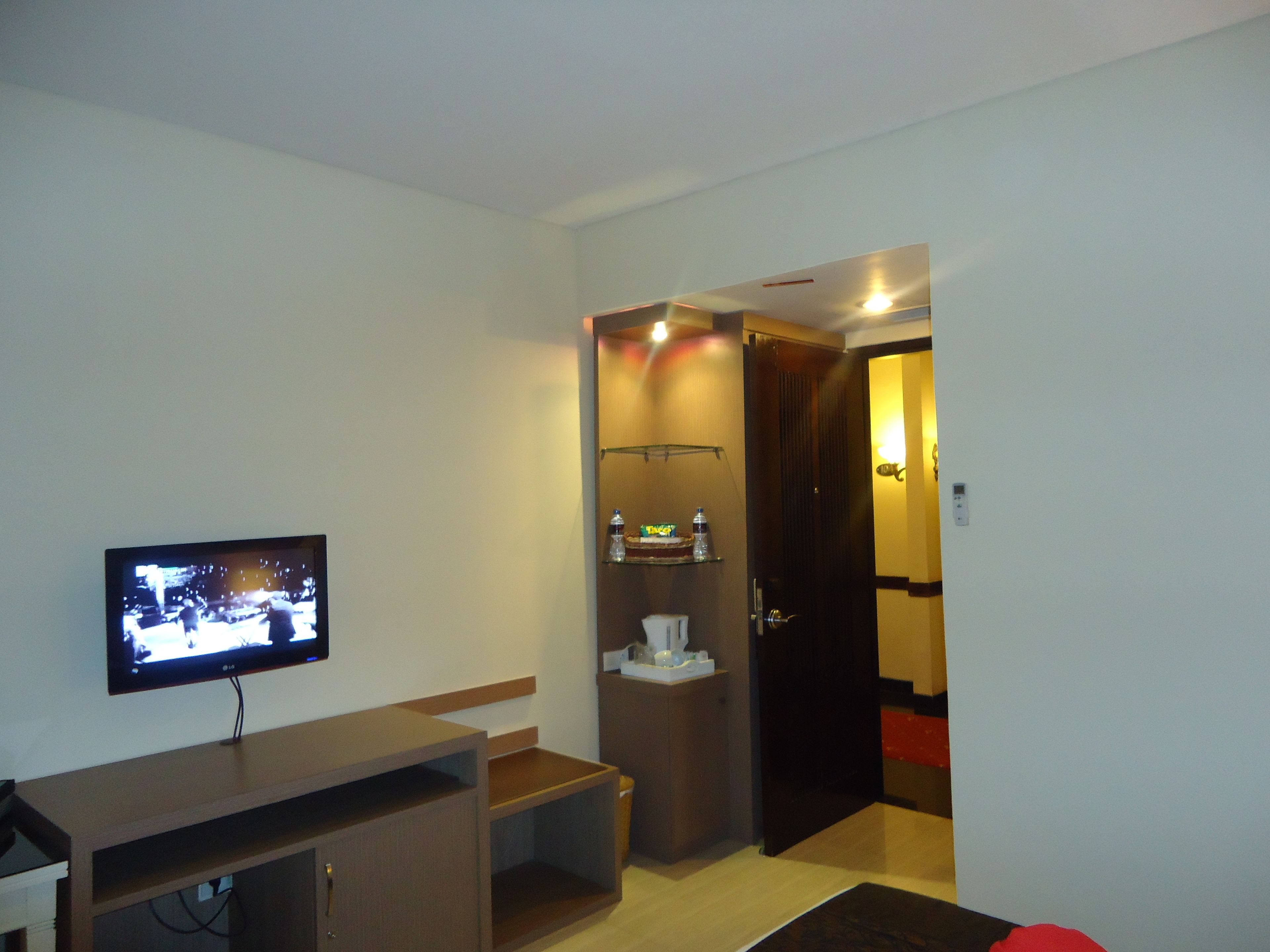 Ein Hotelzimmer mit Fernseher, einem kleinen Schreibtisch, einem Badezimmer inklusive Handtuchhalter und einer Tür zu einem weiteren Raum.