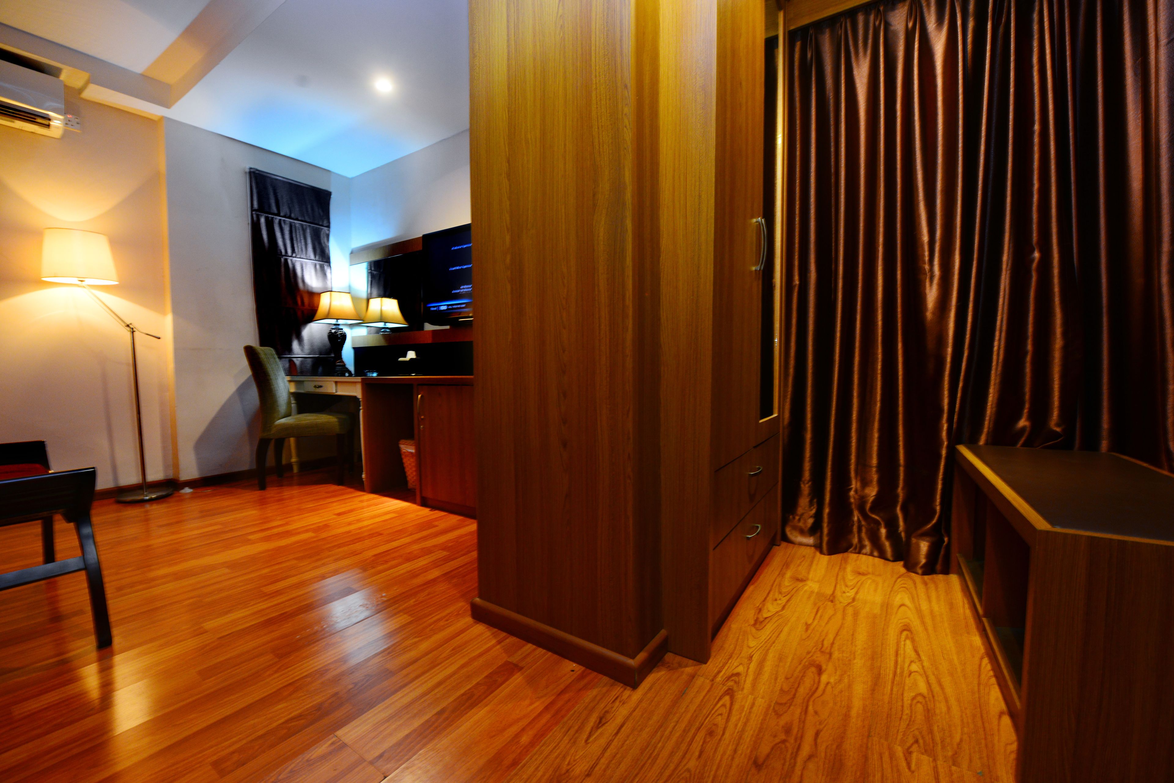 A room with wooden flooring, a desk with a computer, a chair, and a lamp.