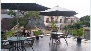 An outdoor patio with tables and chairs, umbrellas, and potted plants. - Hotel Scarlet Makassar (Makassar)