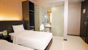 Hotellihuone, jossa on kaksi sänkyä, tumma pääty, lasinen suihkuseinä ja näkyvissä oleva kylpyhuone.