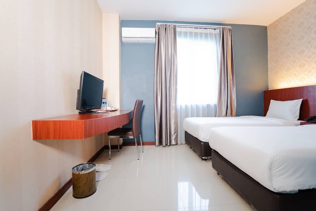 Une chambre d’hôtel équipée d’un bureau, d’une chaise, de deux lits, d’une télévision et d’une fenêtre avec des rideaux.
