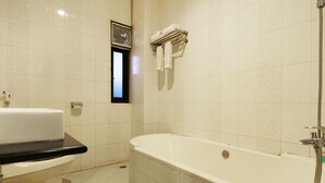 Un baño con bañera, inodoro y una ventana pequeña.
