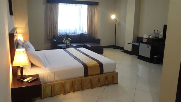 Habitación de hotel con cama, escritorio con lámpara, sofá, escritorio con computadora y ventana con cortinas.