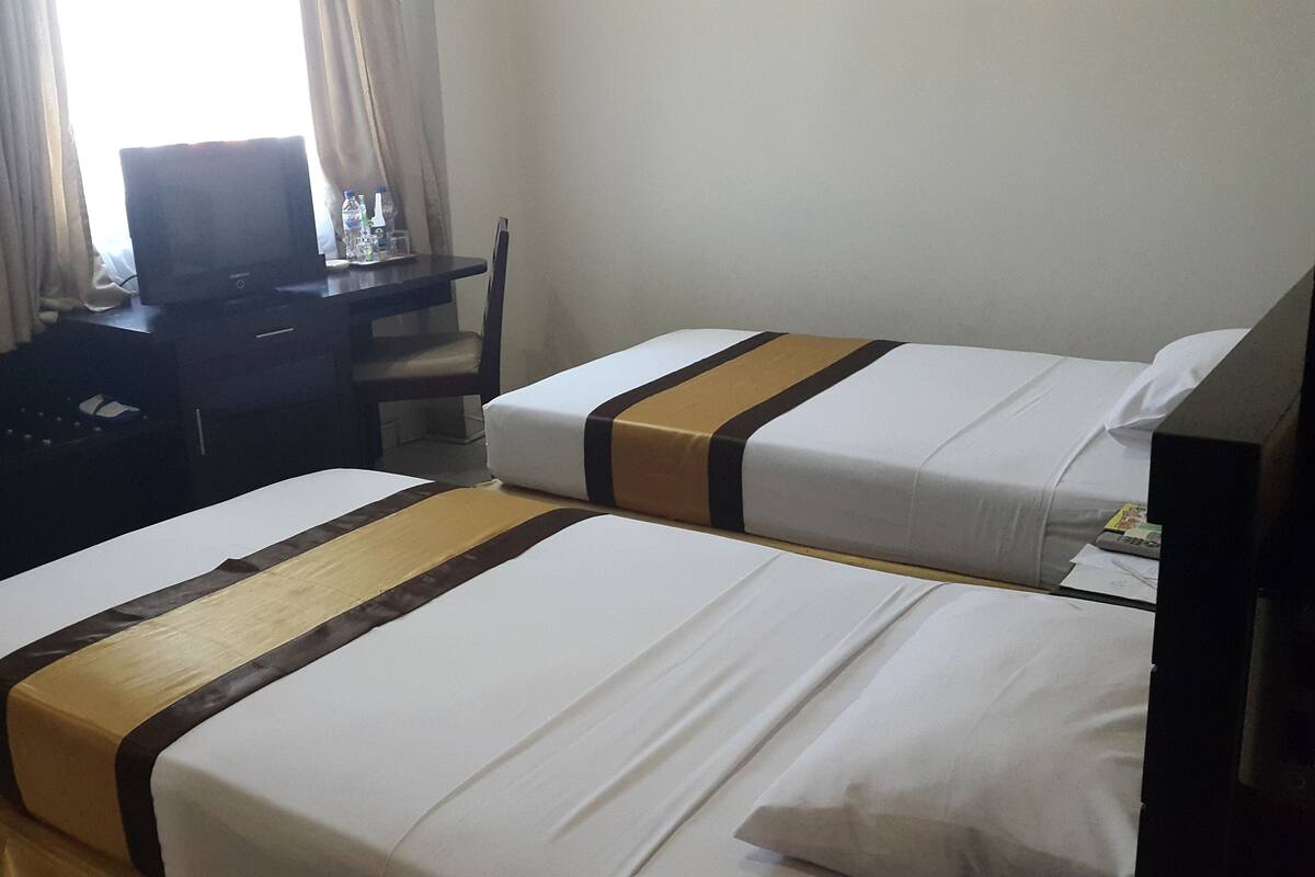 A hotel room with two beds, a desk, a chair, and a television.