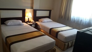 Habitación de hotel con dos camas individuales, una mesita de noche con lámpara, teléfono y televisión.