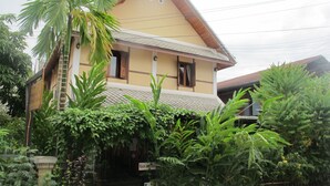 A two-story house with a tiled roof, surrounded by lush greenery and a sign indicating a room is available. - Golden Lotus Place (Luang Prabang)