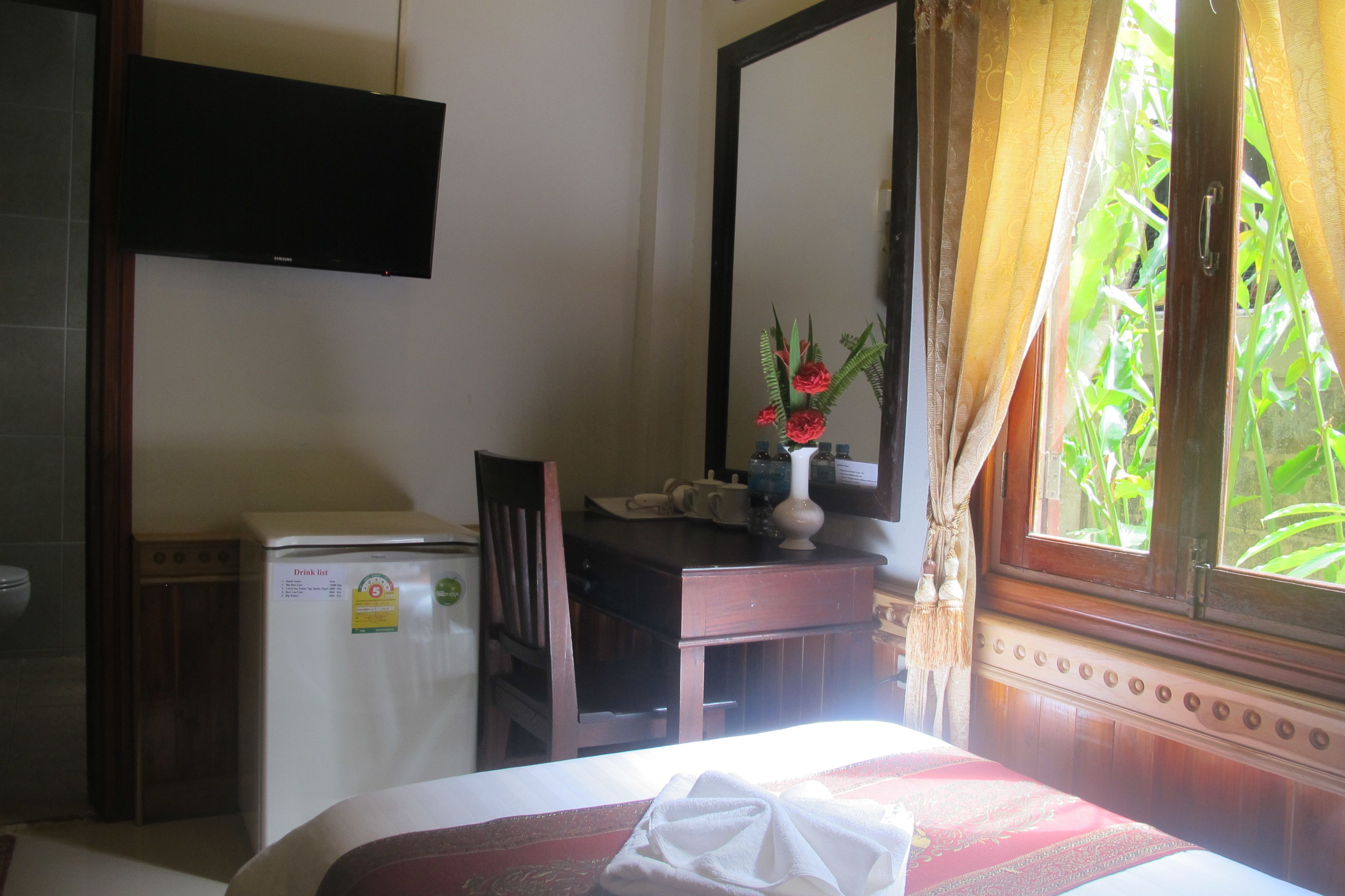 A hotel room with a bed, a desk, a refrigerator, a television, and a window with curtains.
