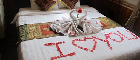 A neatly made bed with a heart-shaped towel arrangement spelling "I love you" and a rose on the bed.