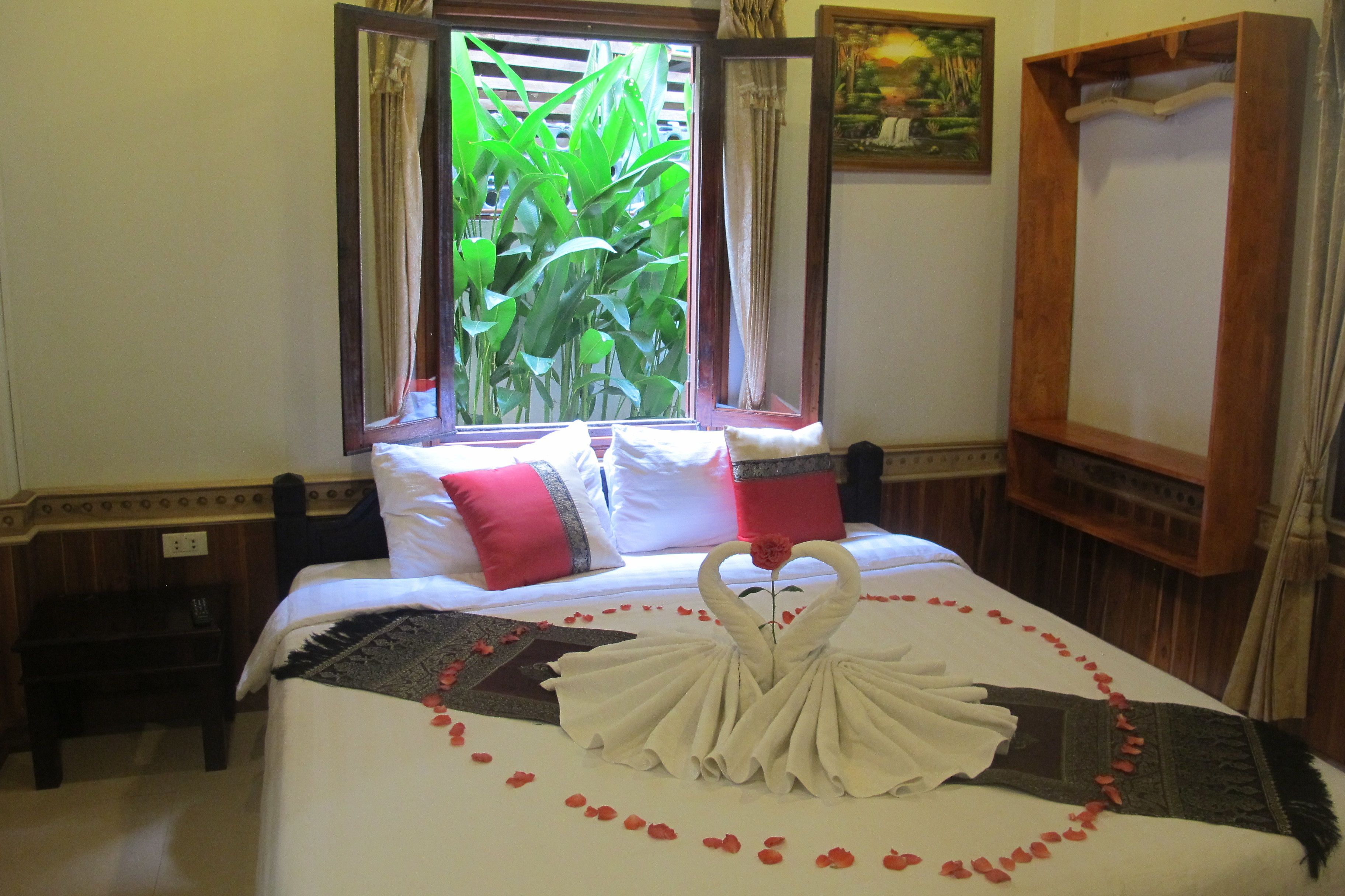 Une chambre d’hôtel avec un lit, une fenêtre avec des rideaux, un tableau au mur et une armoire en bois.