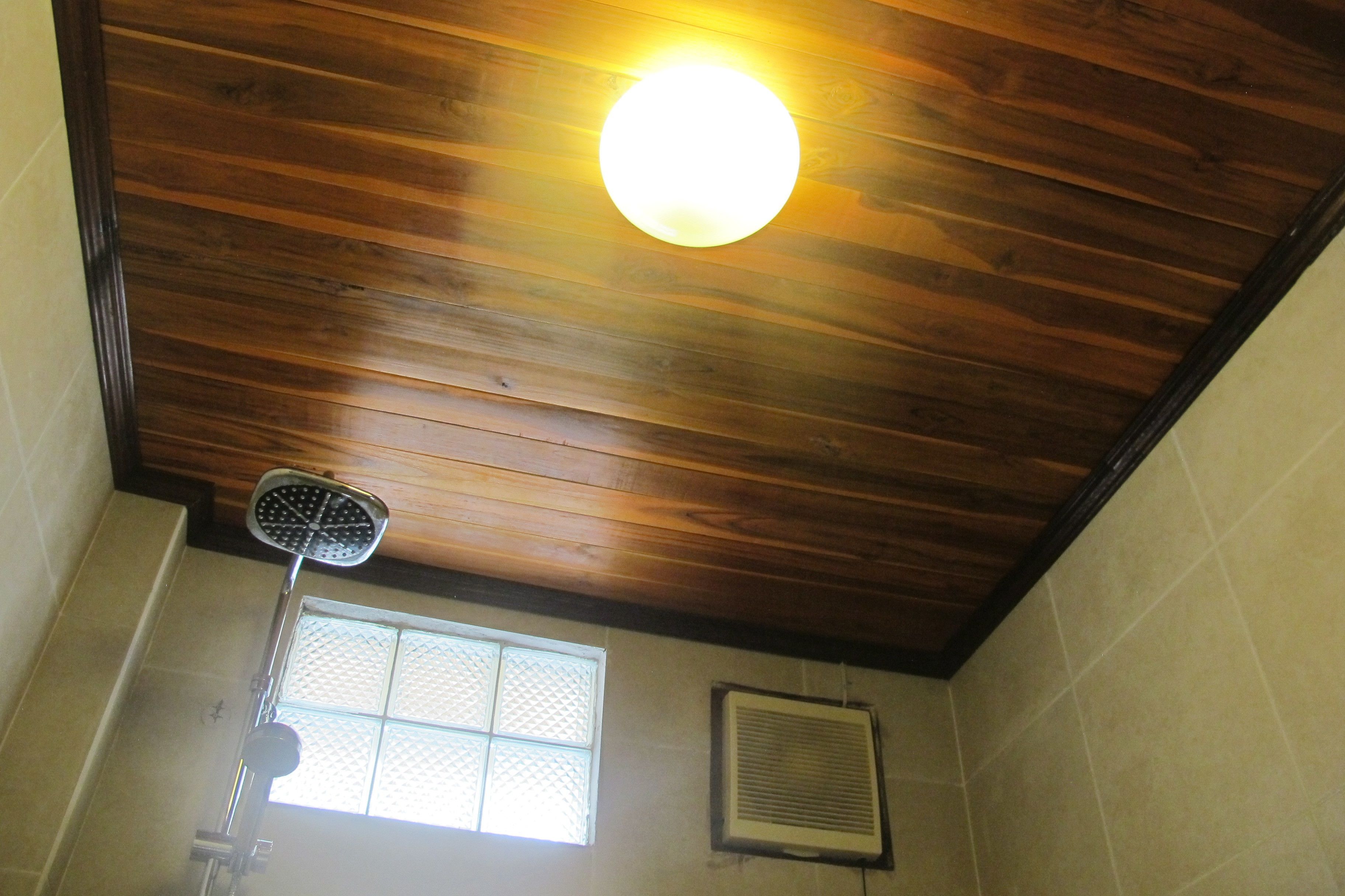 Een kamer met houten plafond, een raam met een rooster en een plafondventilator.