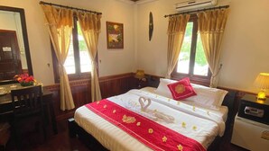 A well-lit bedroom with a wooden ceiling, a bed with a red and white bedspread, a bedside table with a lamp, and a small table with a teapot. - Golden Lotus Place (Luang Prabang)