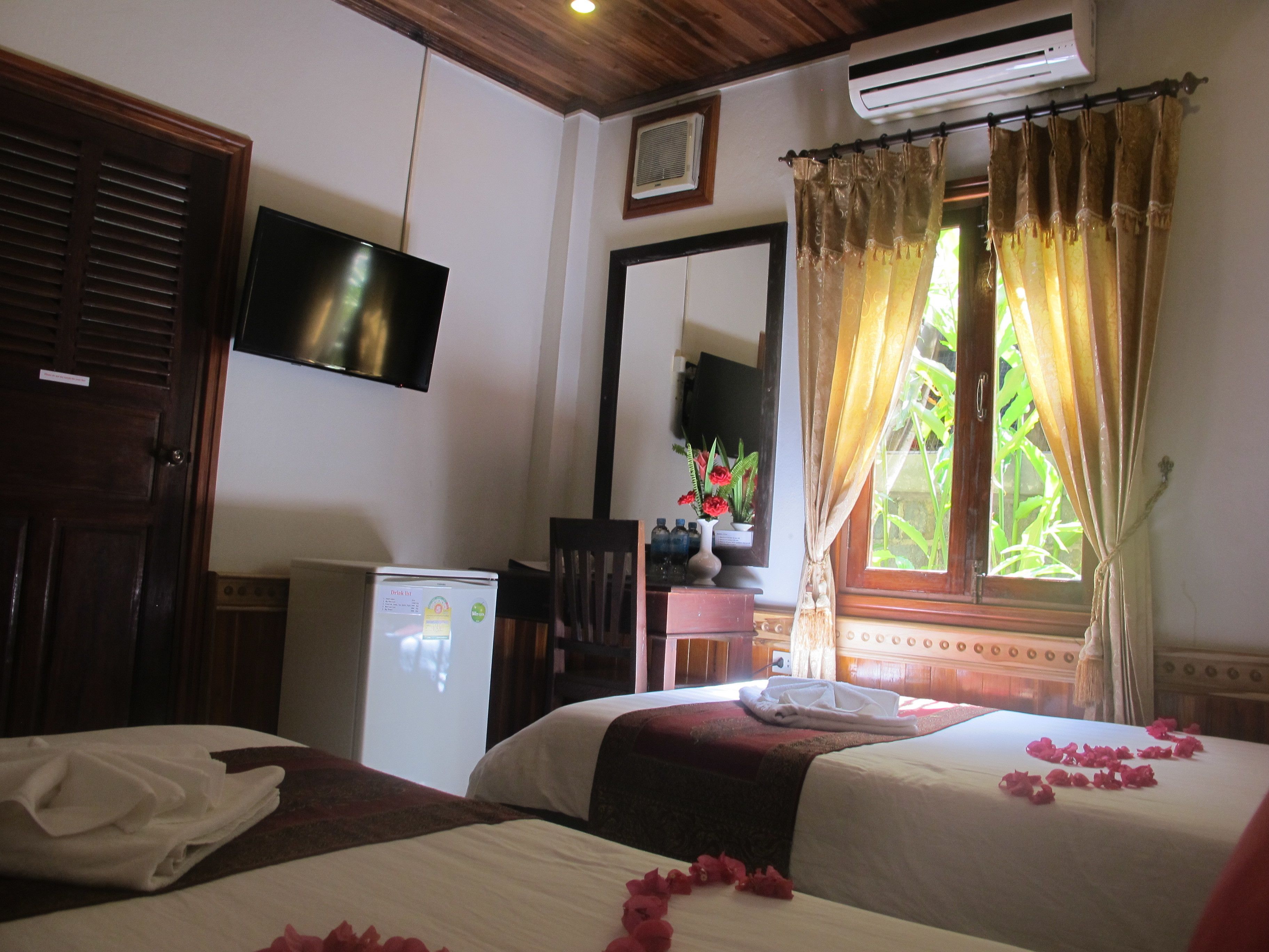 A hotel room with two beds, a television, an air conditioner, and a window with curtains.