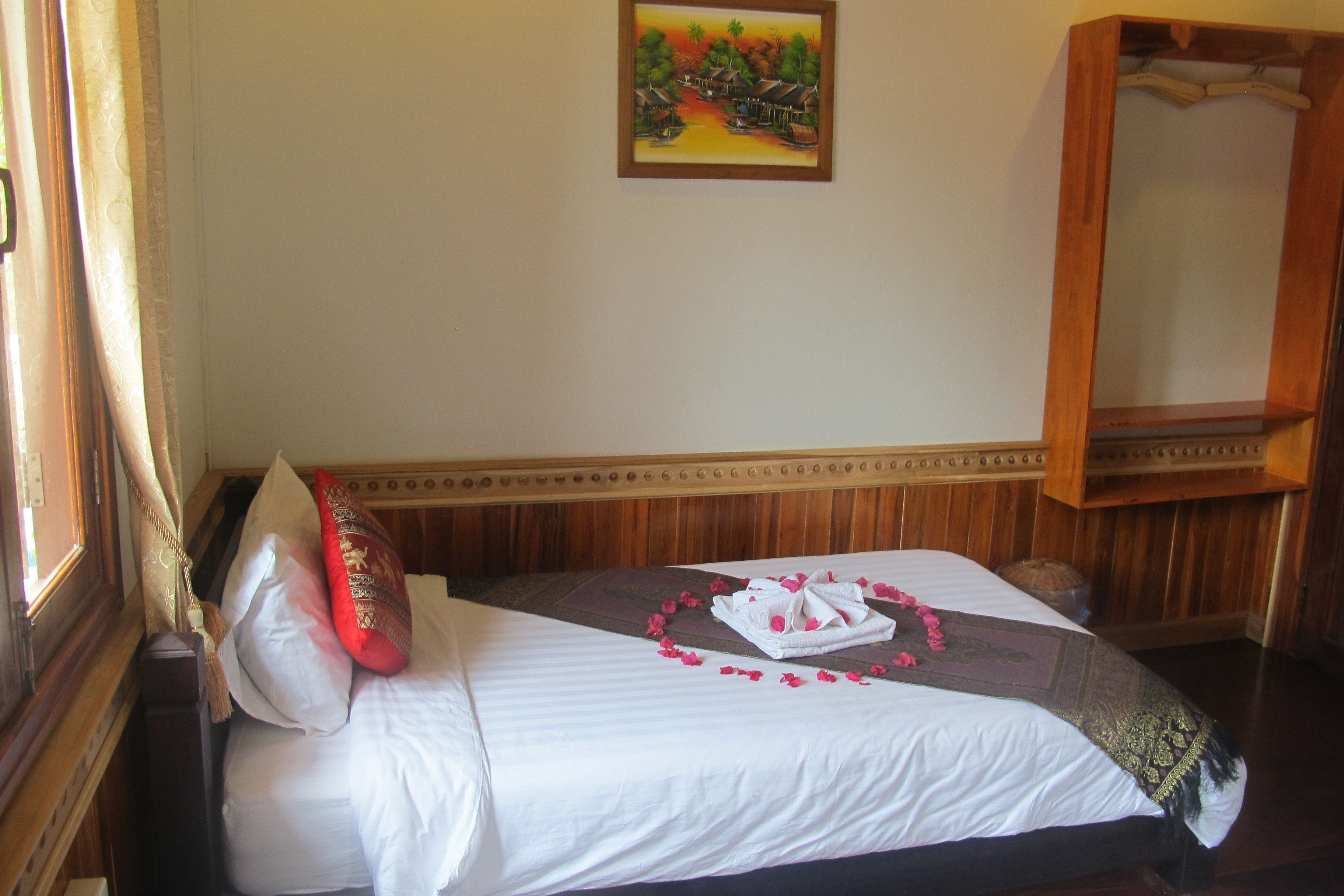 Una cama bien hecha con sábanas blancas, un cojín rojo y una decoración de toallas.