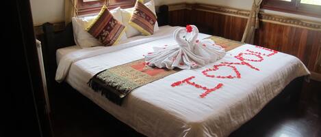 A neatly made bed with a white bedspread, a decorative swan towel, and a heart-shaped arrangement of rose petals spelling "I love you".
