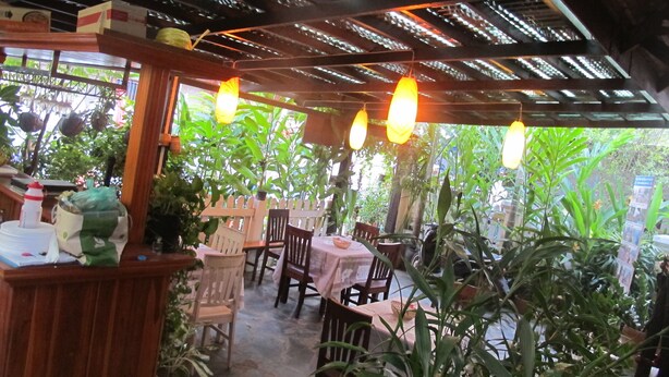 An outdoor restaurant with wooden tables and chairs, surrounded by lush greenery. - Golden Lotus Place (Luang Prabang)