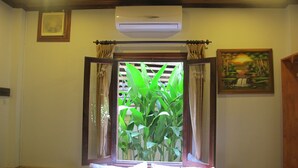 A room with a bed, an air conditioning unit, a window with curtains, and a painting on the wall. - Golden Lotus Place (Luang Prabang)