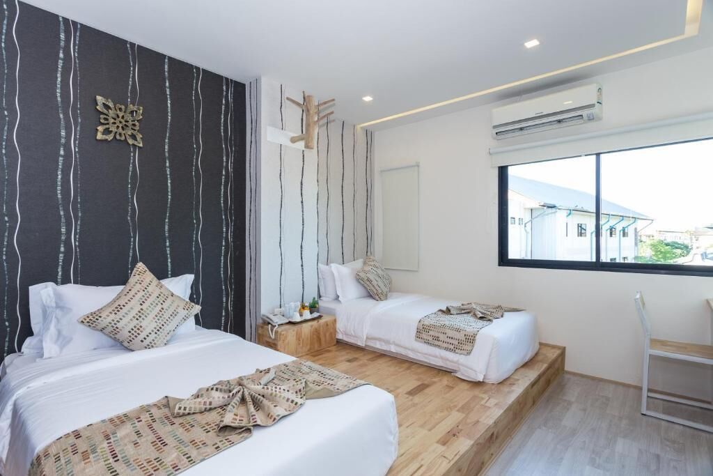 A modern hotel room with two beds, a wooden floor, a large window, and an air conditioning unit.