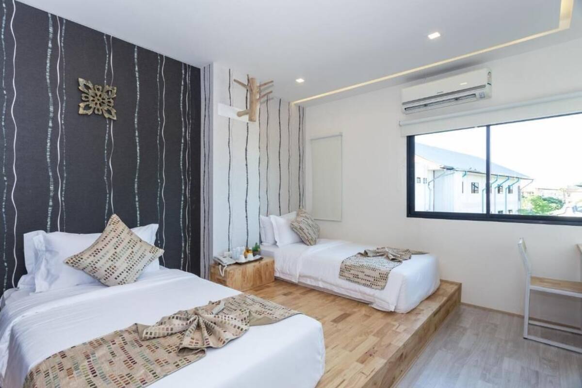 A modern hotel room with two beds, a wooden floor, a large window, and an air conditioning unit.