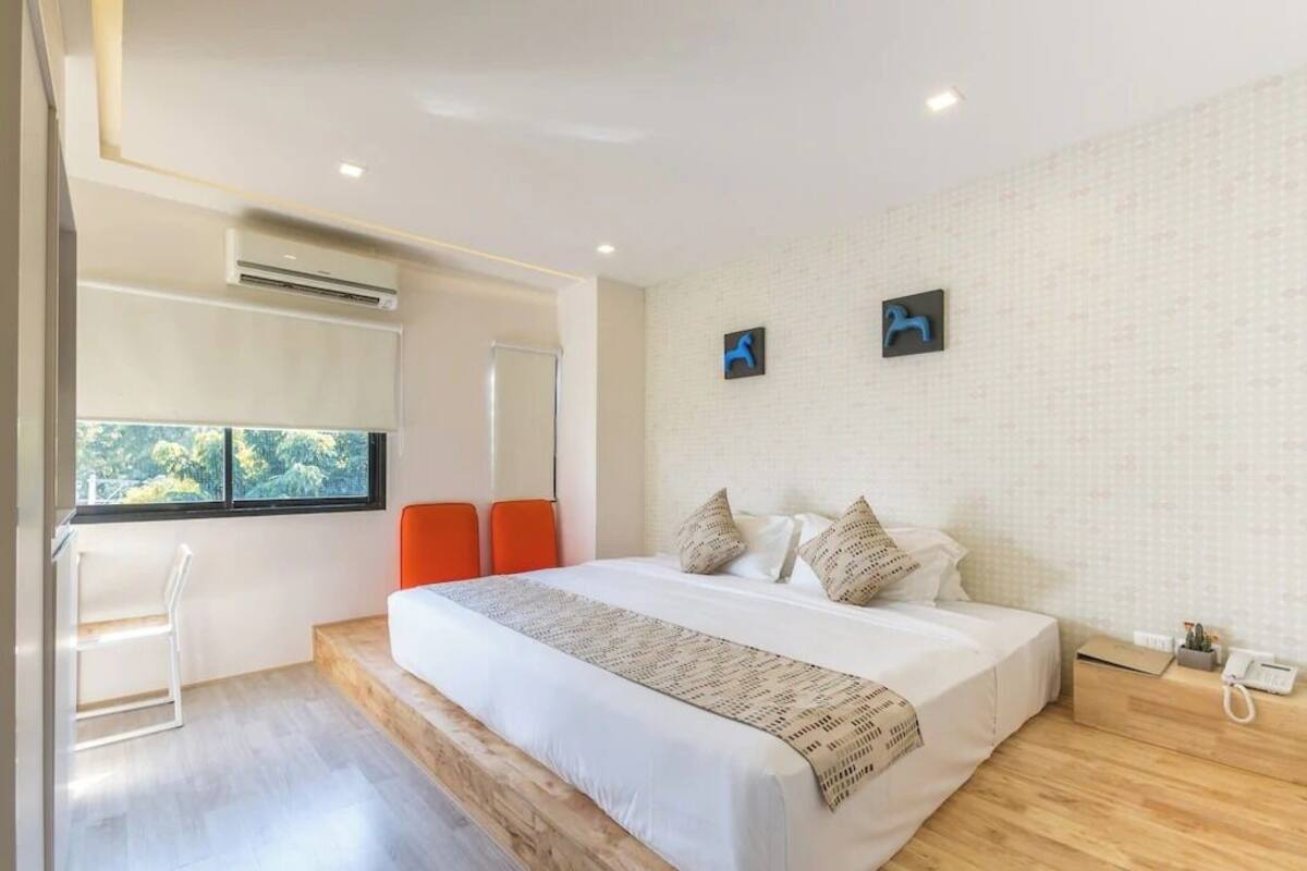 A modern hotel room with a large bed, a desk, and a window with a view of trees.