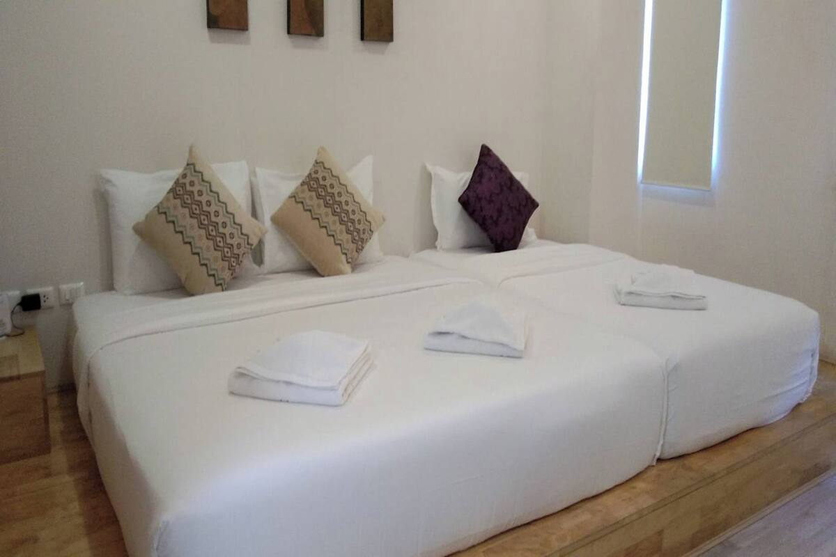 A double bed with white linens, two pillows with patterned designs, and a folded towel on the bed.