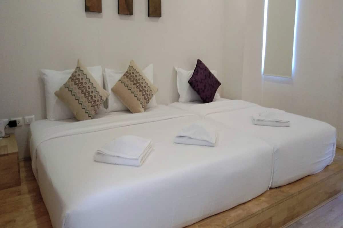 A double bed with white linens, two pillows with patterned designs, and a folded towel on the bed.