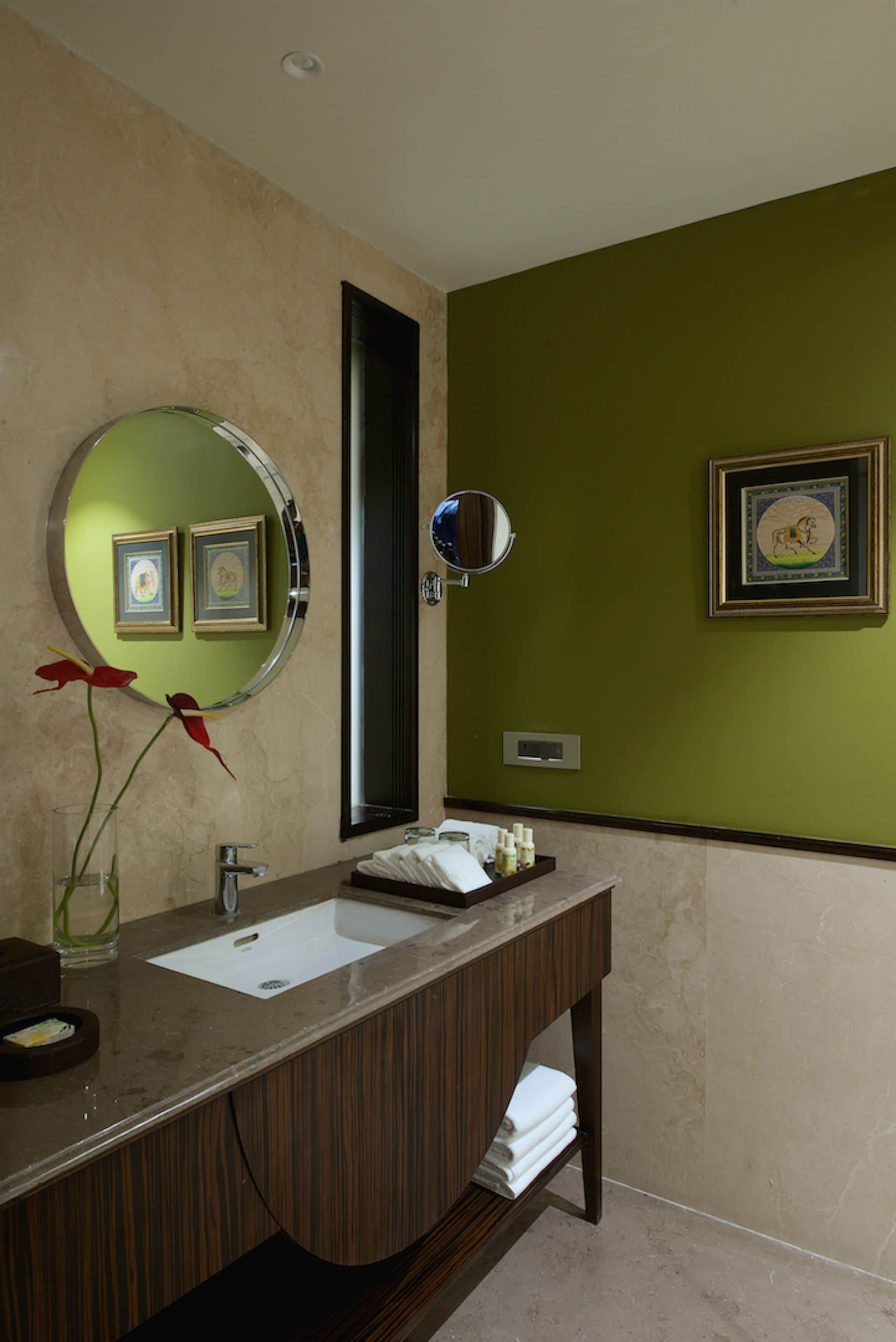 A bathroom with a vanity, mirror, framed pictures, and a vase with red flowers.