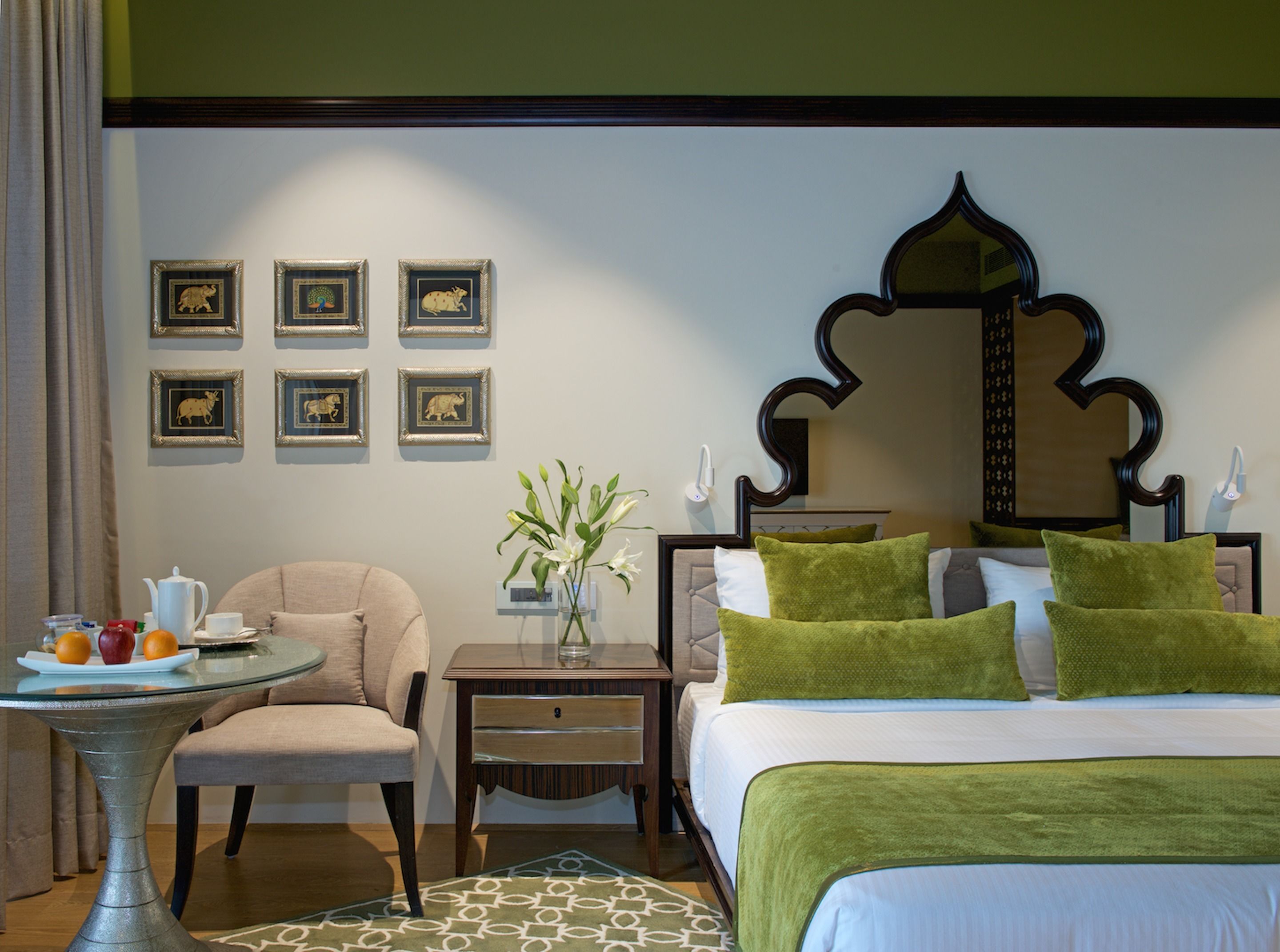 A hotel room with a bed, a chair, a small table with a vase of flowers, and framed pictures on the wall.