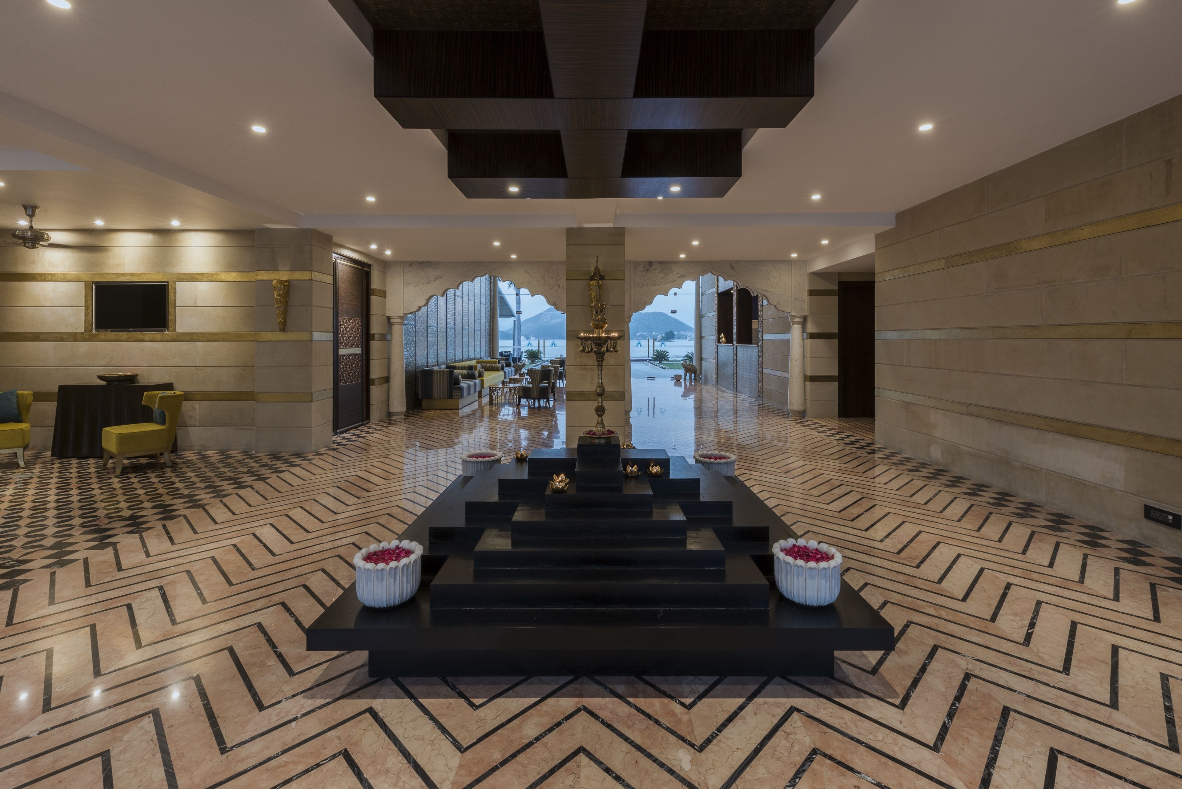 A spacious lobby with a central staircase, a chandelier, and a large window offering a view of the outdoors.