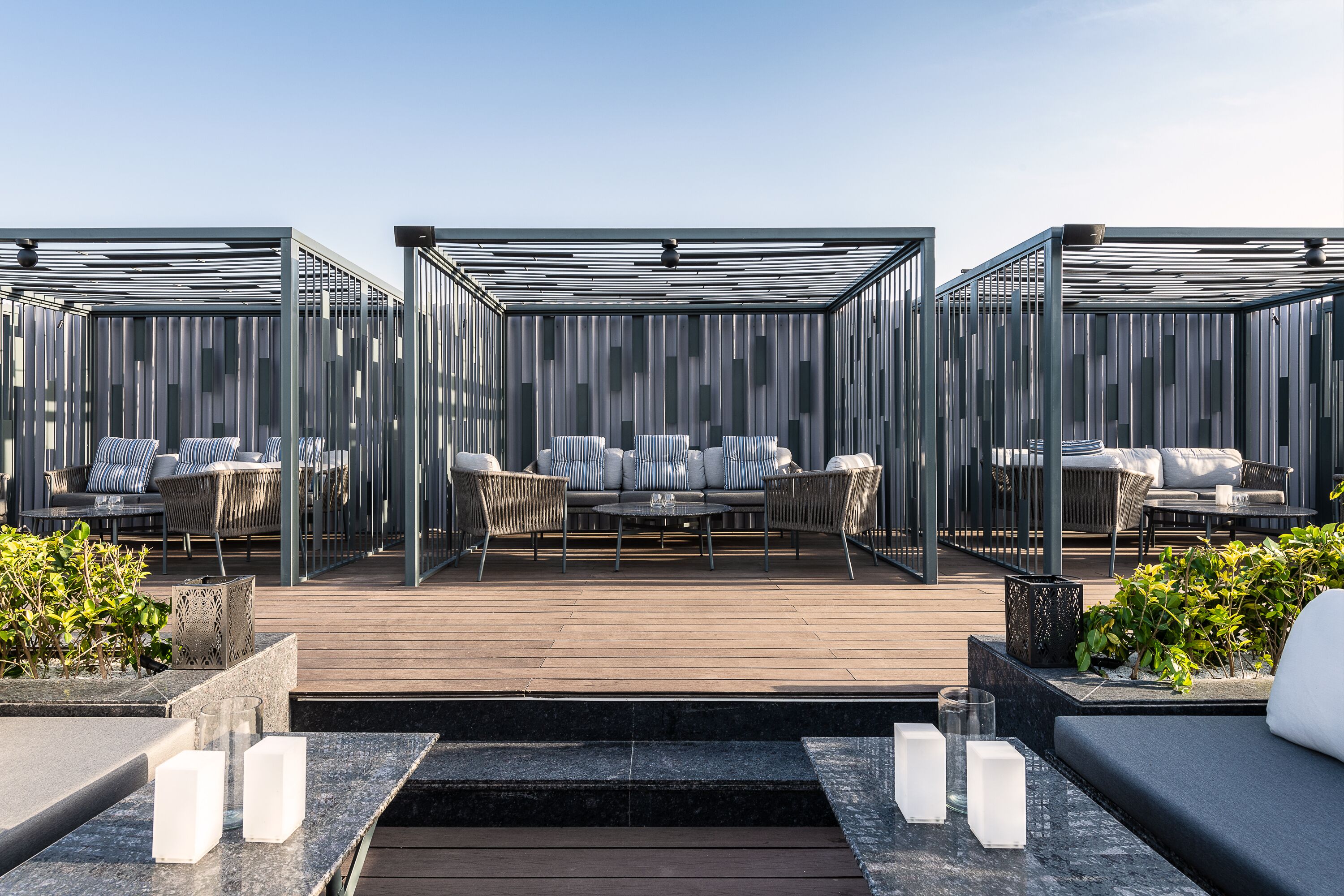 Terraza en la azotea con cubierta de madera, zona de estar exterior con sofás y sillones, y estructura de cerramiento de vidrio.