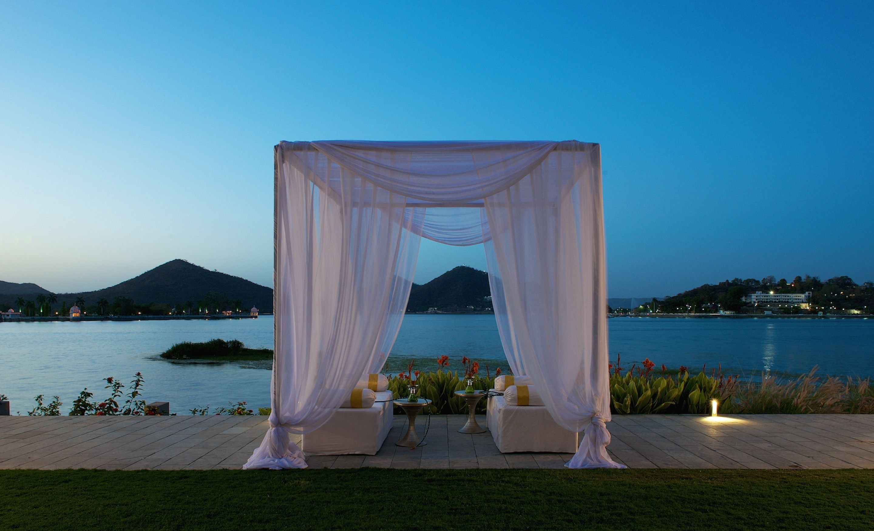 An outdoor wedding setup with a white canopy and seating, overlooking a body of water and distant hills.