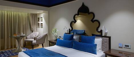A hotel room with a large bed, a desk, a chair, and a small table with a vase of flowers.