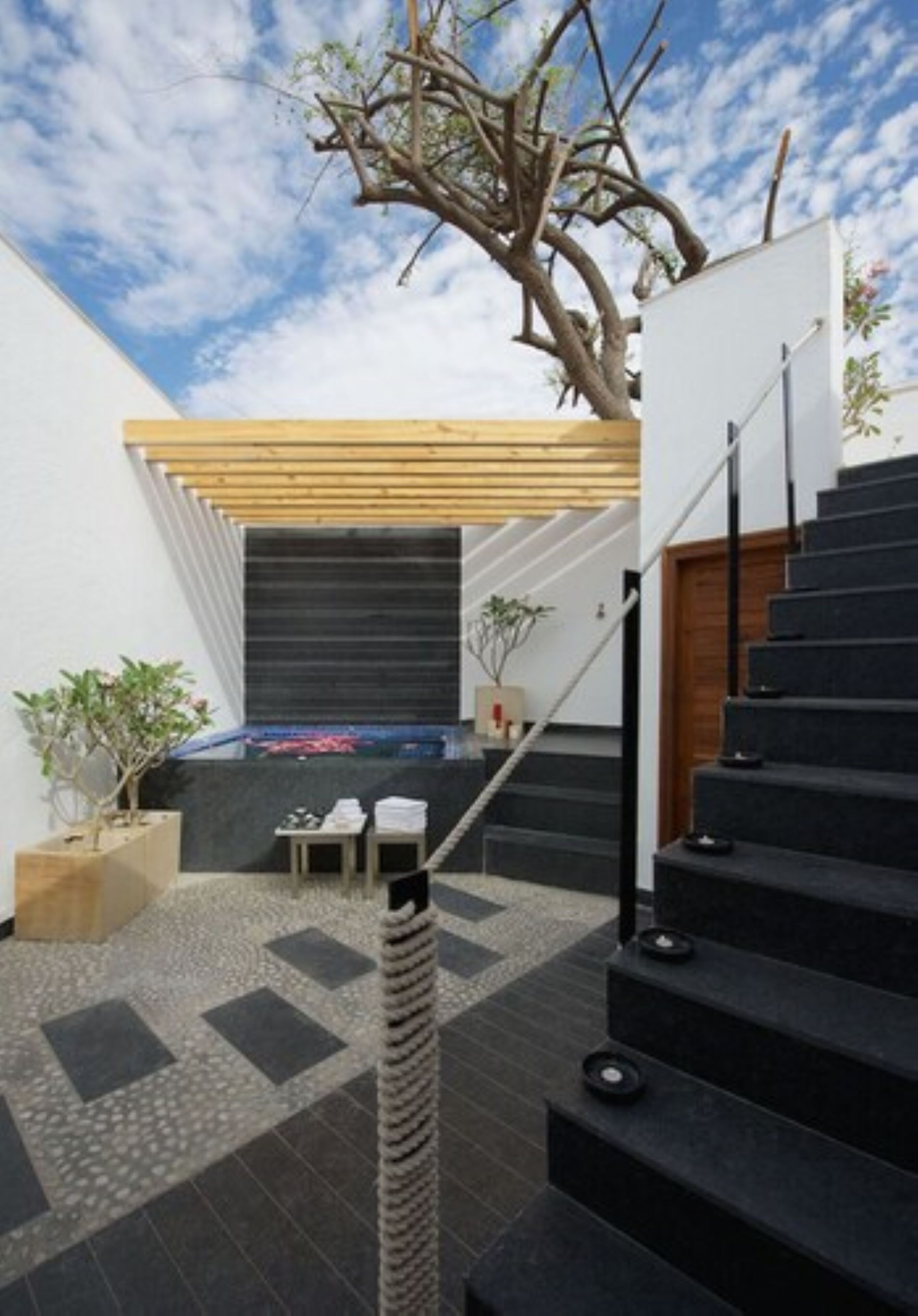 A modern outdoor staircase leading to a covered area with a wooden deck and a black door.