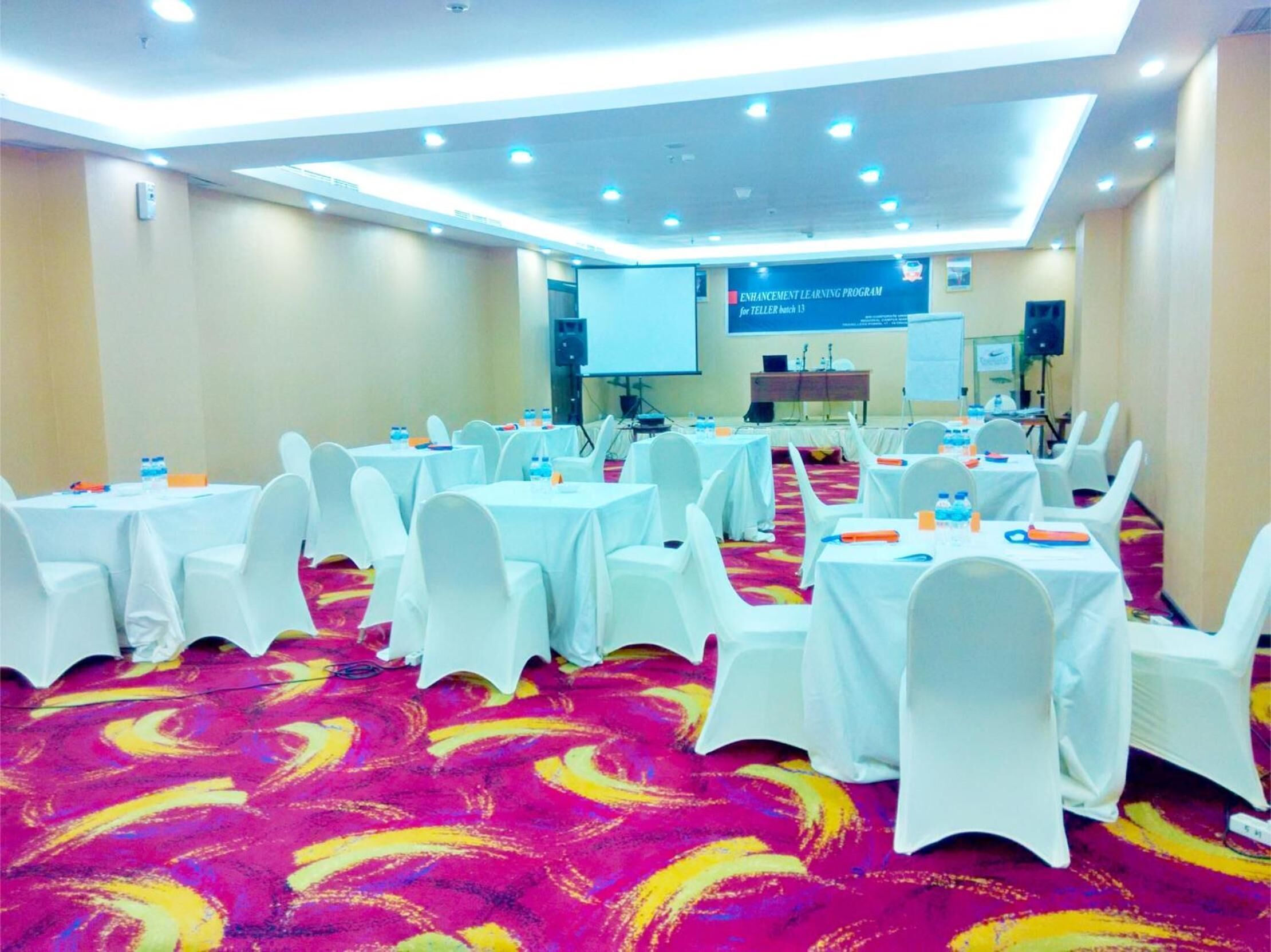 A conference room with tables and chairs, a projector screen, and a carpeted floor.
