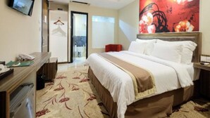 A hotel room with a bed, a desk, a chair, a TV, and a painting on the wall. - Travellers Hotel Phinisi (Makassar)