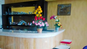 A bar area with a counter, stools, and flower arrangements. - Travellers Hotel Phinisi (Makassar)