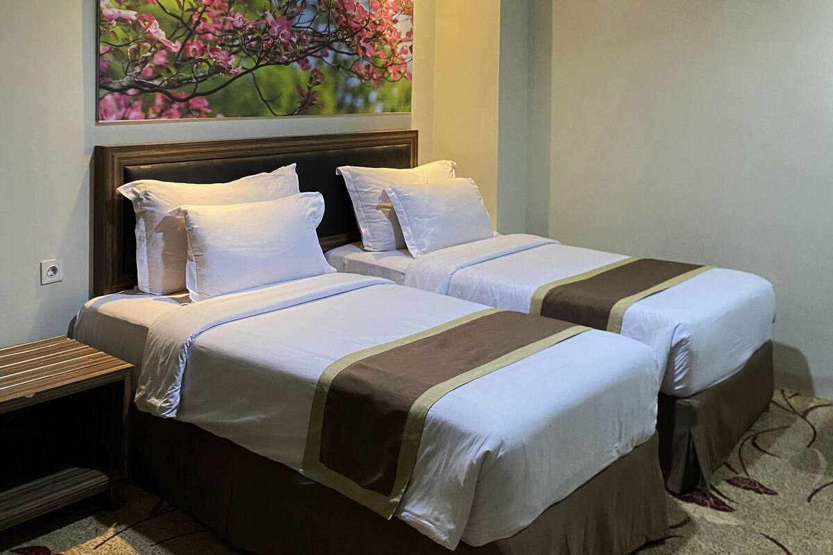 Habitació d'hotel amb dos llits, una tauleta de nit, un quadre amb flors i una catifes amb motius florals.