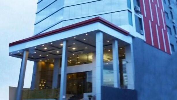 A modern hotel with a curved facade, multiple floors, and a prominent entrance with a covered area. - Travellers Hotel Phinisi (Makassar)