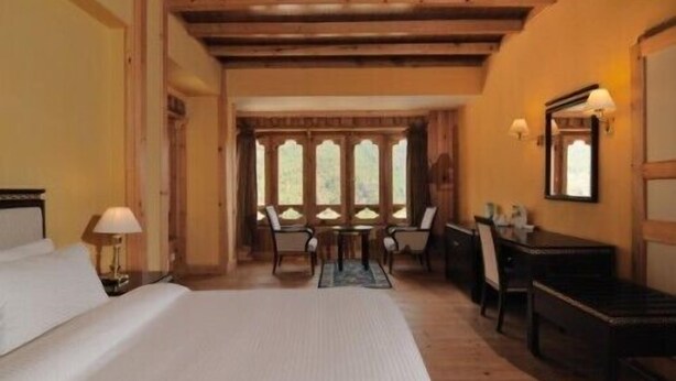A hotel room with a bed, a desk, and a chair. There are windows with a view of trees. - Taktsang Boutique Resort & Spa (Paro)