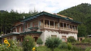 A traditional multi-story building with ornate architectural details, surrounded by lush greenery and mountains. - Taktsang Boutique Resort & Spa (Paro)