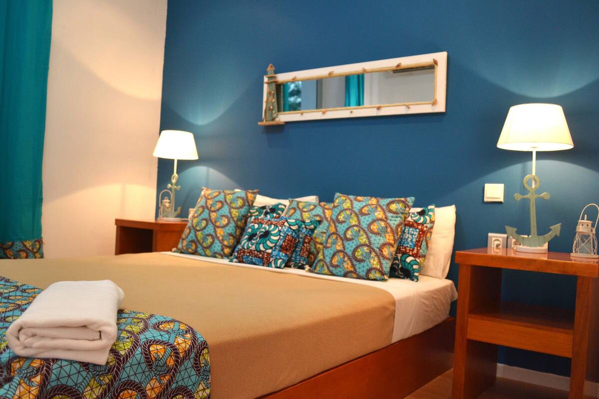 A hotel room with a bed, two bedside tables, a nightstand, a mirror, and a lamp.